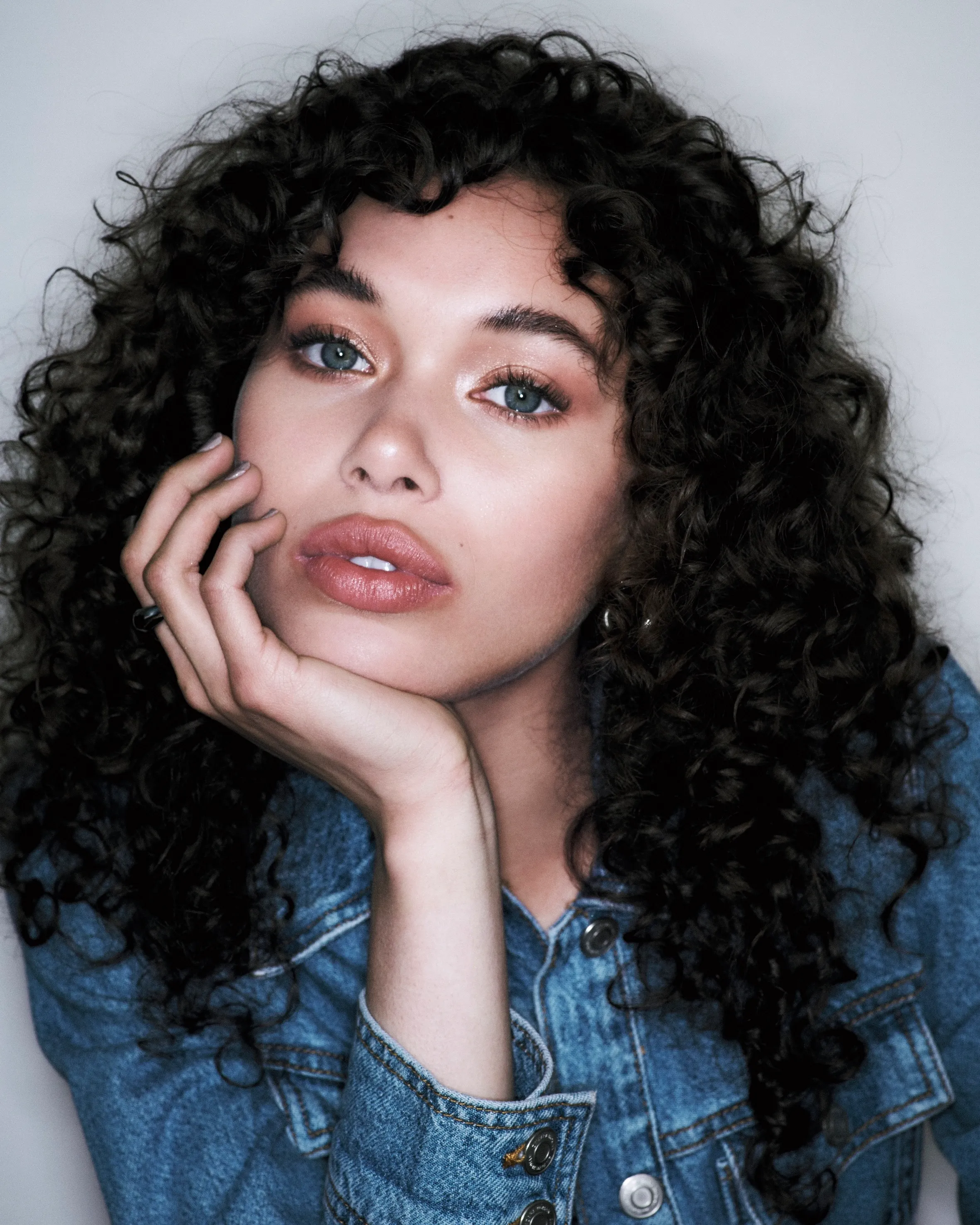 Woman in a denim jacket with defined, bouncy blowout curls and a relaxed, editorial expression.