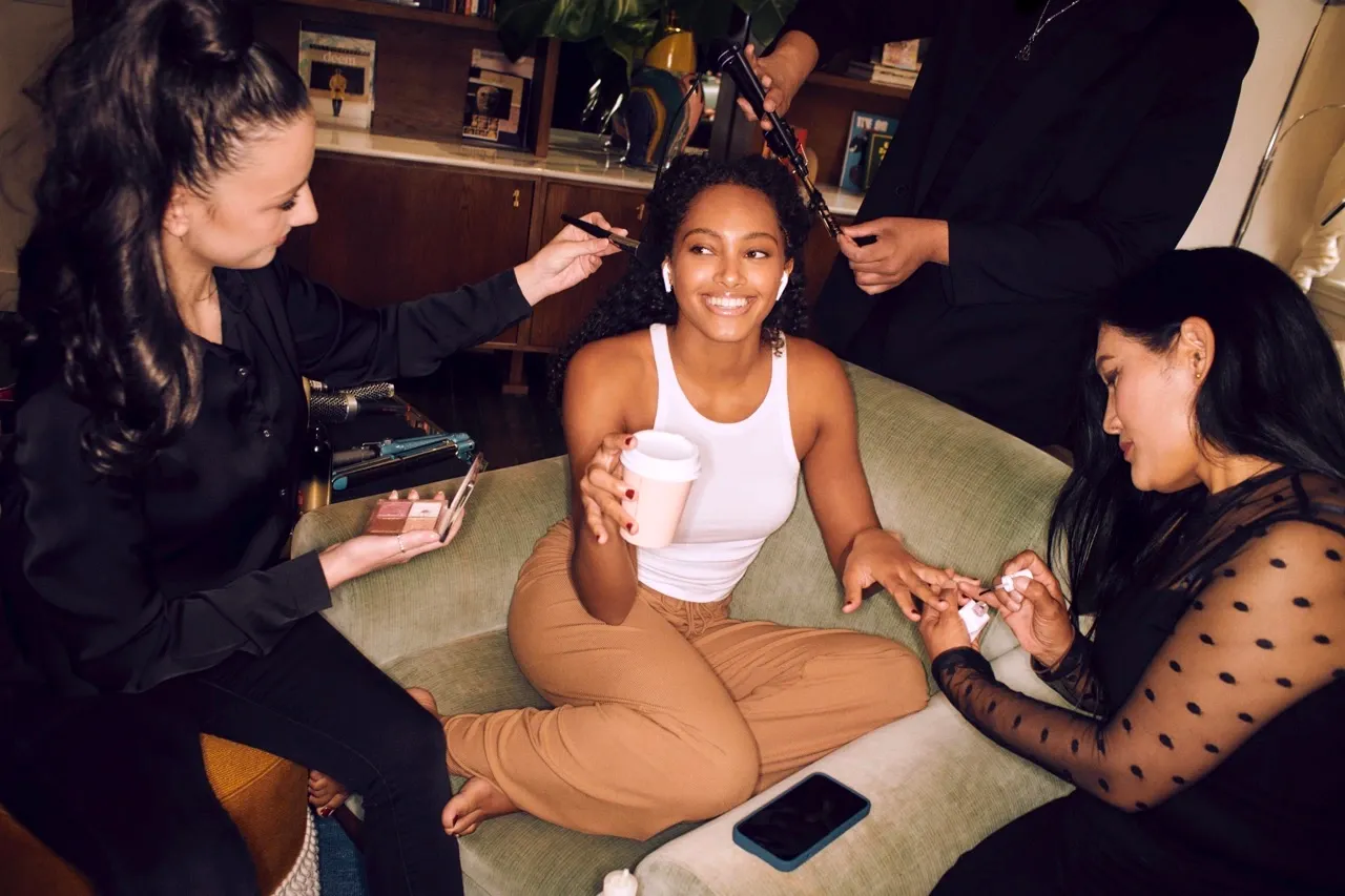 French polish on toes while smiling model enjoys coffee and hair styling on a couch
