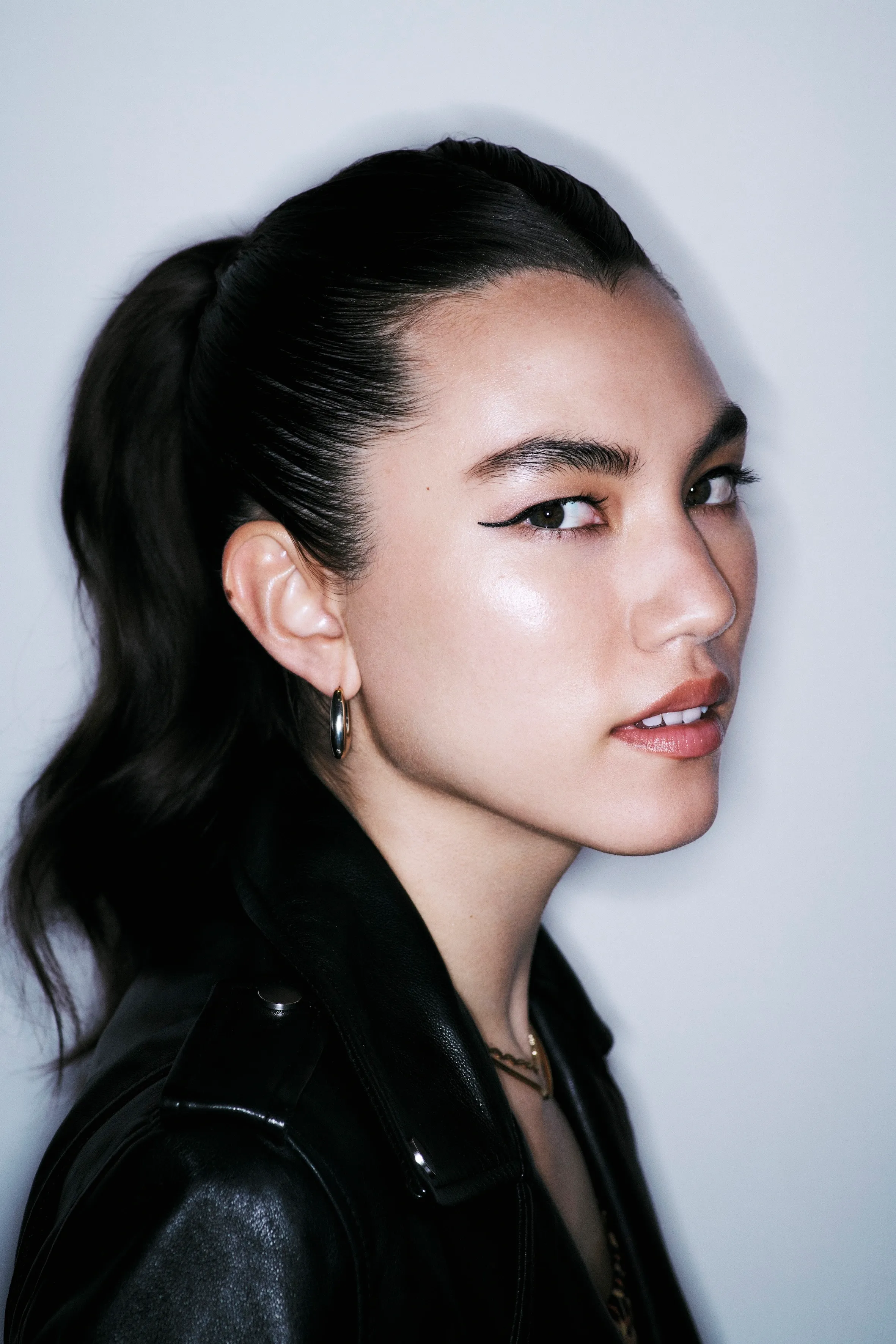 Sleek, pulled-back romantic updo on a woman in a leather jacket, shot in sharp side profile with winged liner.
