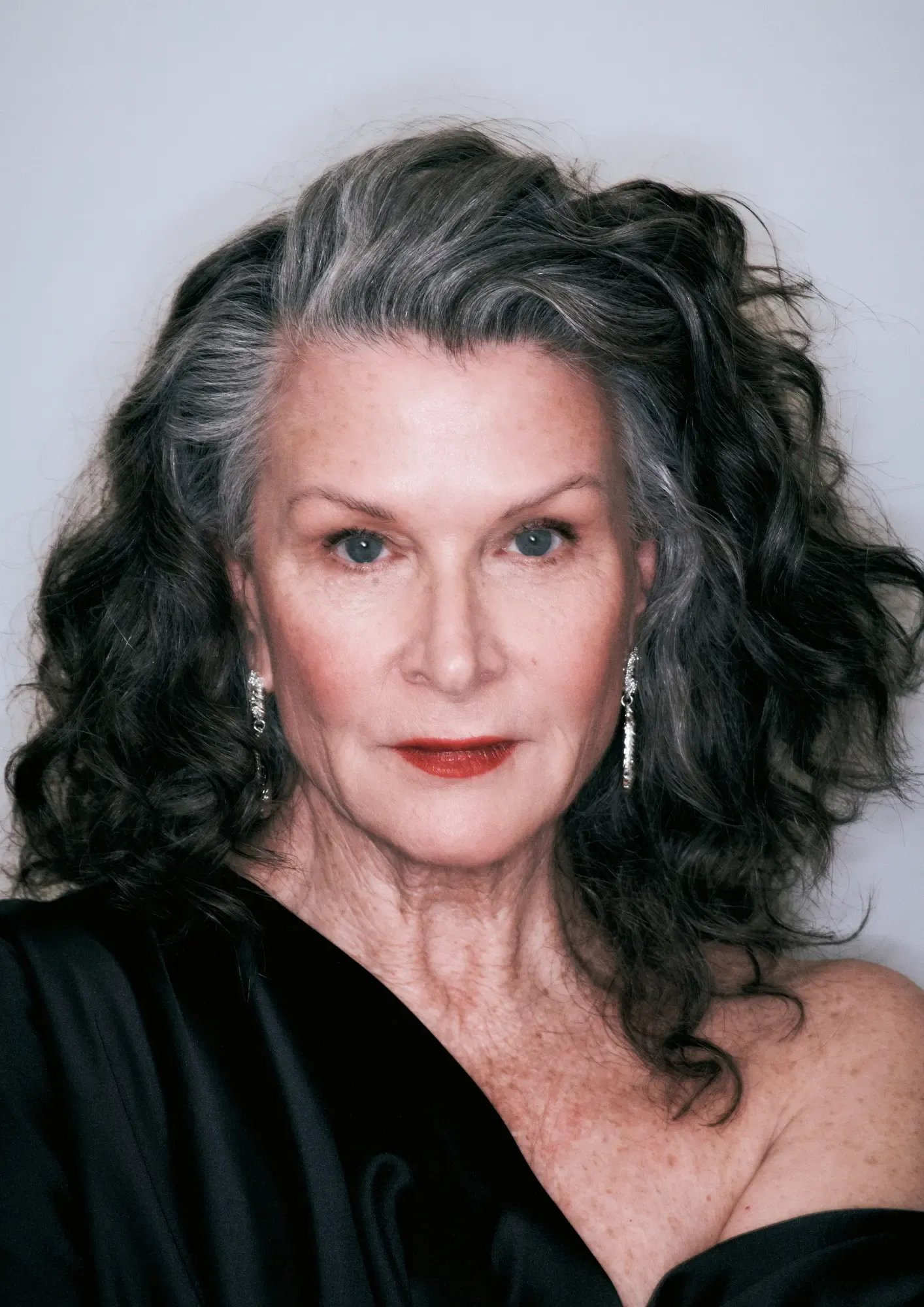 An older woman with beautifully styled silver and dark curls and red lips, wearing a signature blowout that exudes timeless elegance.