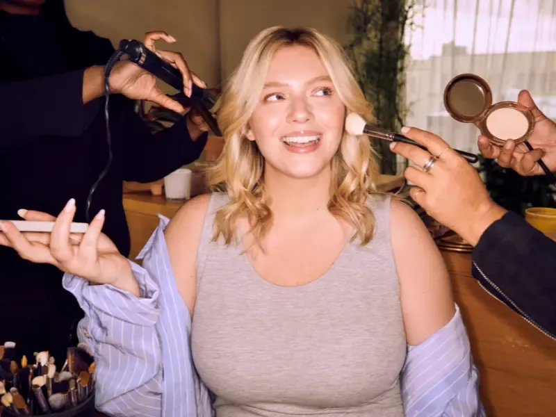 At home blowout styling session with a woman getting her hair curled and makeup applied by professionals.