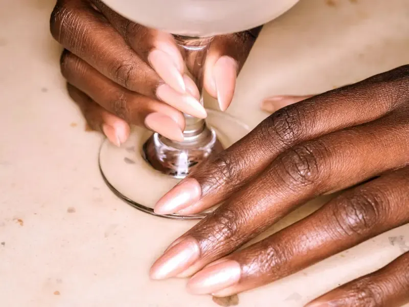 At-home manicure with long, almond-shaped nude nails holding the base of a wine glass.