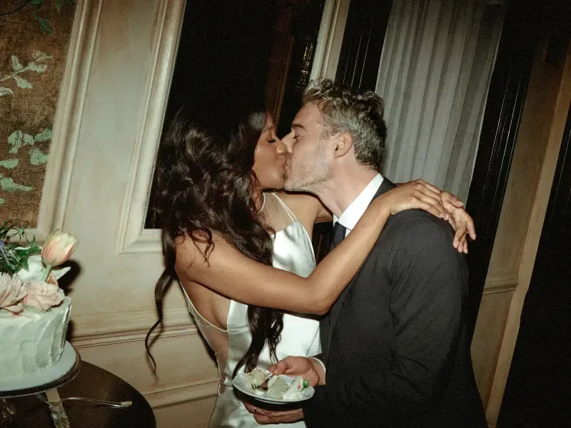 At home silk press giving the bride smooth, shiny waves as she kisses her groom beside a wedding cake