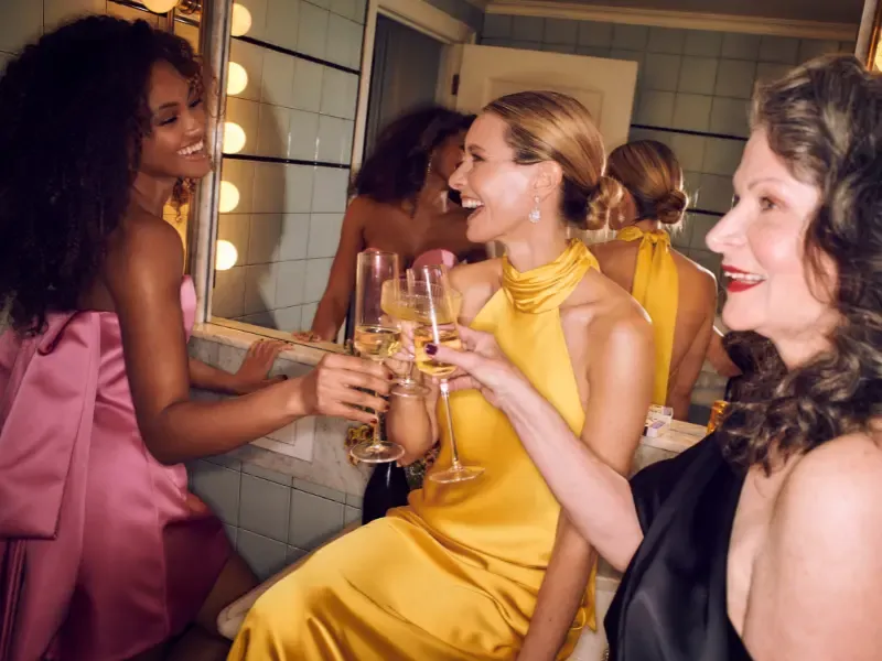 Bridal party makeup looks flawless as three women in elegant dresses toast with champagne in a glamorous bathroom setting