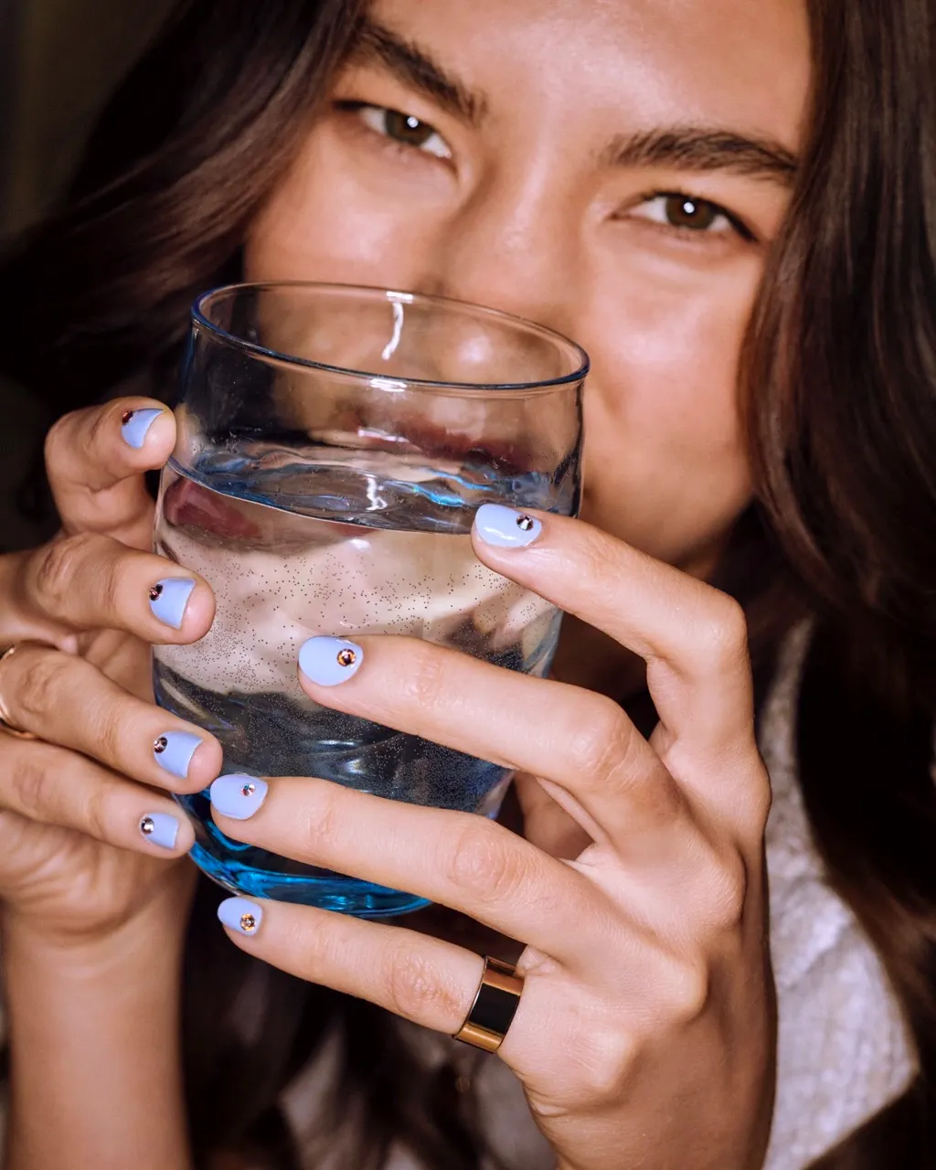 Gel manicure upkeep shown with blue polished nails holding a clear glass of water.