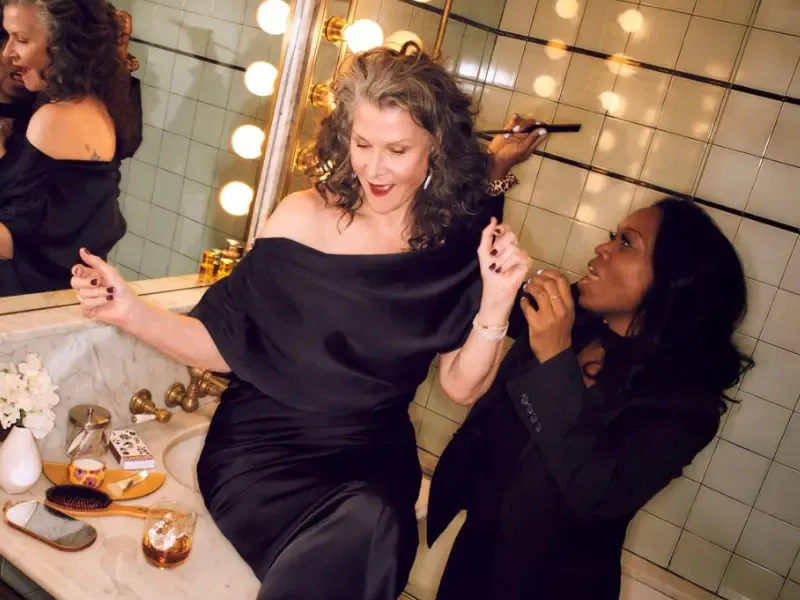 Hair blowout for volume on older woman in black satin dress enjoying glamorous bathroom touch-up.