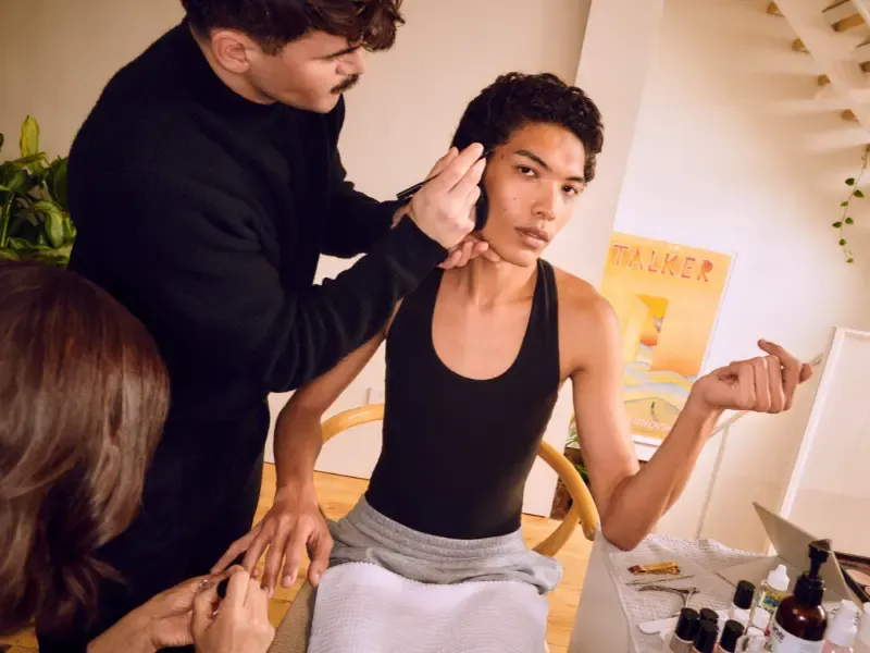 Hair styling for events with a stylist applying makeup and grooming details to a person seated in a modern home studio.