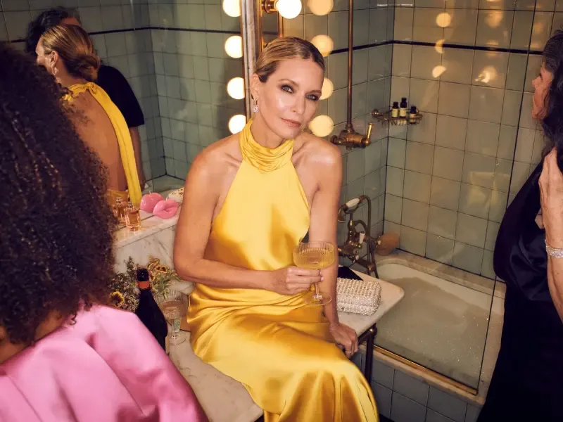 Makeup trial results on an elegant woman in a yellow satin gown holding a champagne glass in a glamorous vanity bathroom setting
