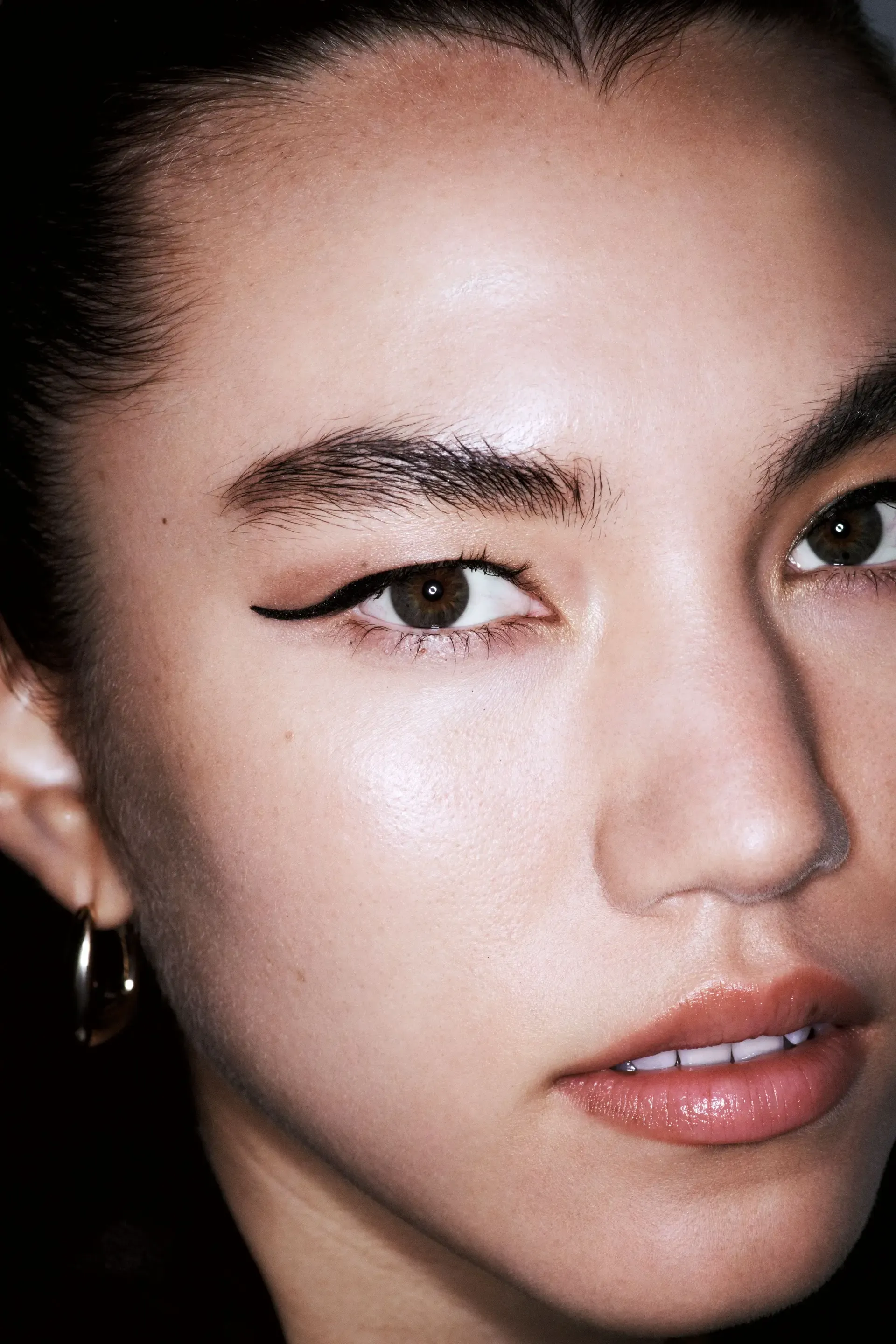 Minimalist wedding makeup featuring sharp black eyeliner and glowing skin in a close-up beauty portrait.