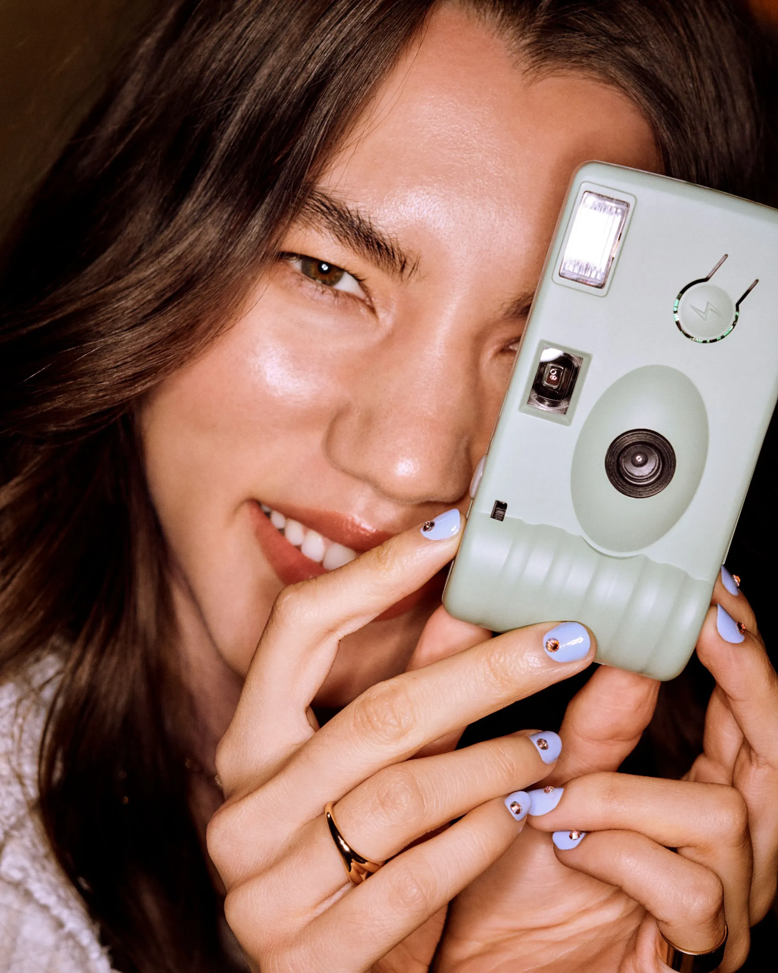 Nail care and design shown with close-up of blue nails with gem accents as woman holds a vintage camera.