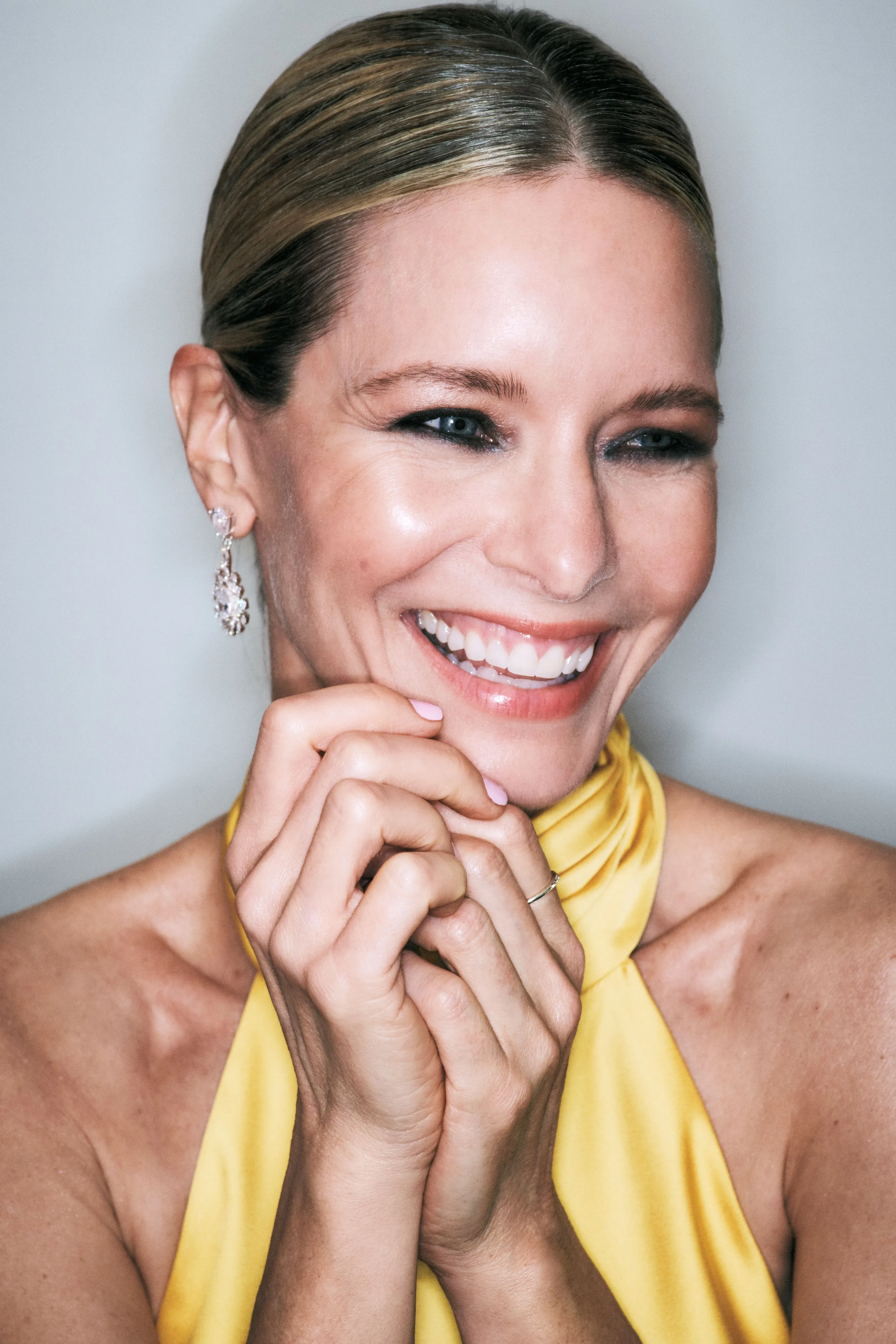 Silk press at home delivers a sleek center-parted updo on a smiling woman wearing diamond earrings and a yellow halter dress.