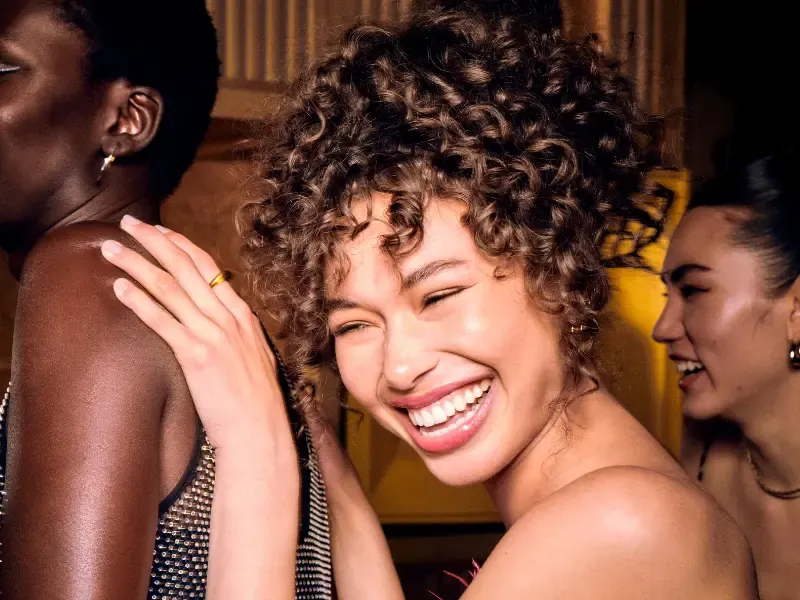 Updo hairstyles on women dancing and smiling at a lively party with elegant curls and pinned hair.